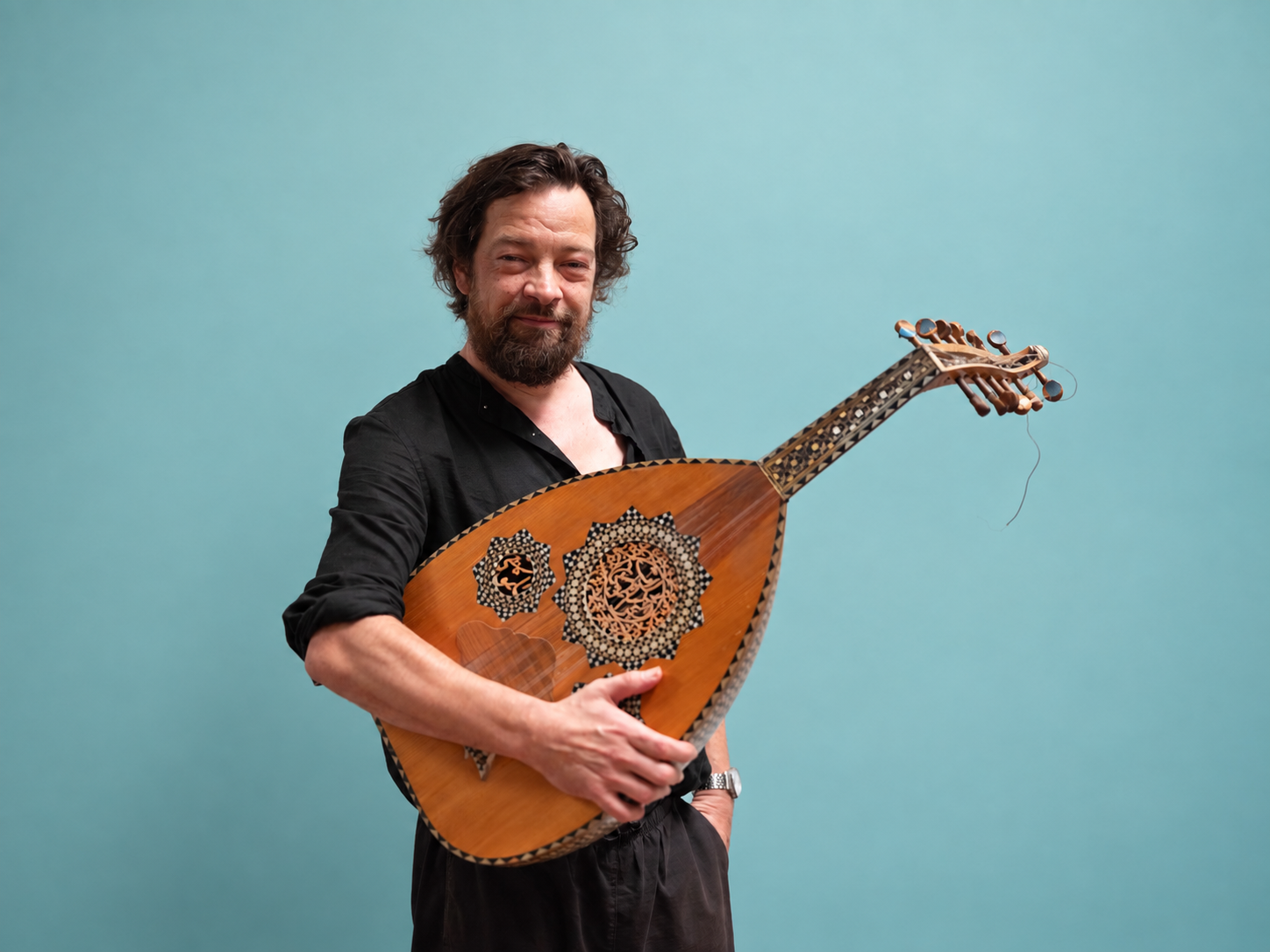 Peter Verhelst holding an ornate oud against a blue-green background